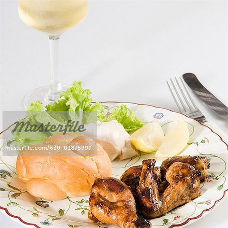 Close-up of roasted chicken and bun in a plate with a glass of wine