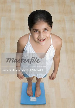 High angle view of a girl standing on a weighing scale and smiling