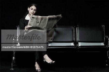 Businesswoman sitting on a bench and reading a newspaper