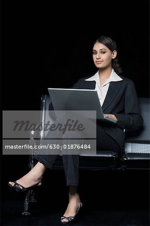 Portrait of a businesswoman sitting on a bench and using a laptop