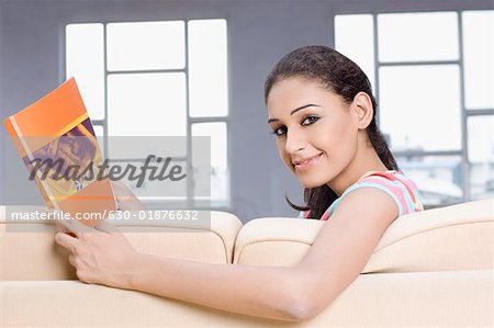 Portrait of a young woman sitting on a couch and holding a magazine
