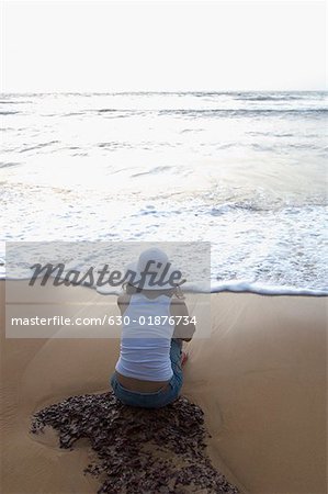 Rear view of a young woman sitting on the beach, Goa, India