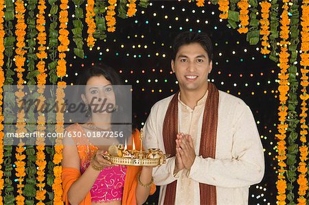 Portrait of a young woman holding a diwali thali with a young man standing beside her