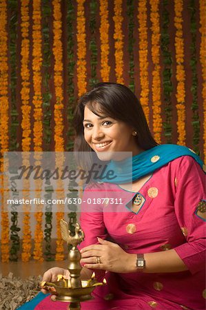 Portrait of a young woman lighting a diwali lamp and smiling
