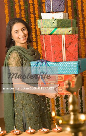 Portrait of a young woman holding a stack of diwali gifts and smiling