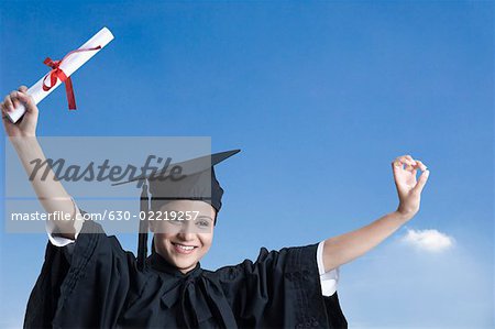 Portrait of a young female graduate holding a diploma with her arms raised and smiling