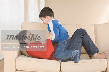Young woman lying on a couch and playing with her son