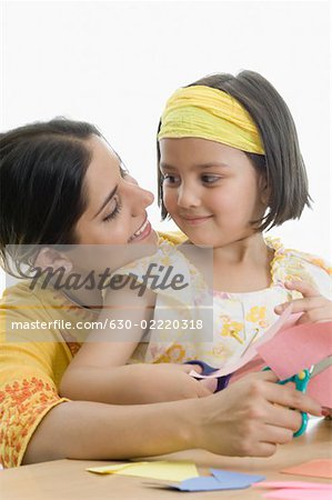 Young woman with her daughter cutting papers with scissors