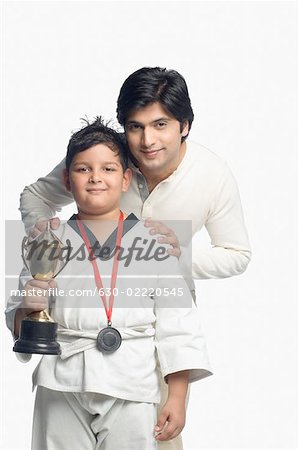 Portrait of a boy holding a trophy with his father standing behind him