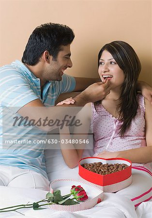 Man feeding candy to his girlfriend on the bed
