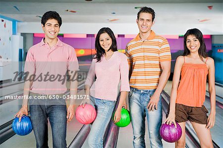 Two young couples holding bowling balls in a bowling alley