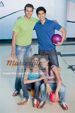 Two young couples with bowling balls in a bowling alley