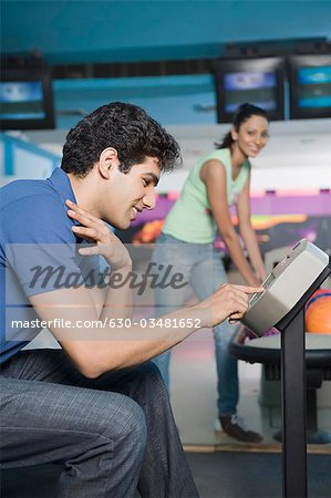 Young man operating the control panel and his friend looking at him in a bowling alley