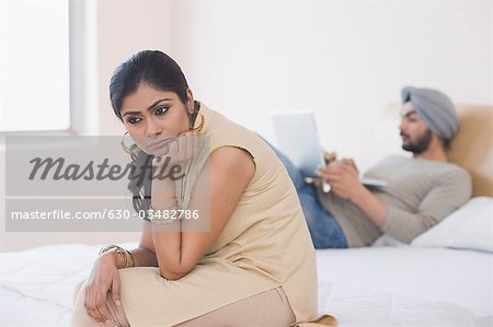 Woman looking sad while her husband working on a laptop on the bed