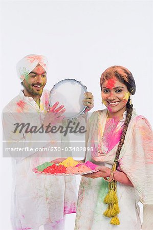 Man playing a tambourine with a woman holding a tray of Holi colors