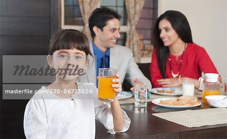 Portrait of a girl holding a glass of milk with her parents in the background
