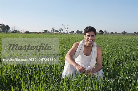 Farmer crouching in the field and smiling, Sonipat, Haryana, India