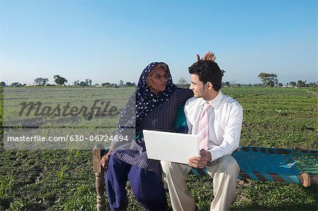 Businessman sitting in the field near his mother and using a laptop, Sonipat, Haryana, India Businessman sitting in the field near his mother and using a laptop, Sonipat, Haryana, India