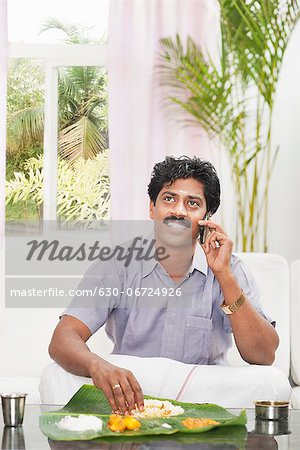 South Indian man having food and talking on a mobile phone