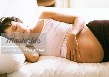 Pregnant woman with eyes closed, lying on side on bed