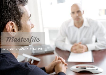 Businessmen sitting at desk, clasping hands