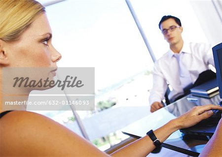 Businesswoman sitting at desk with businessman, side view, close-up