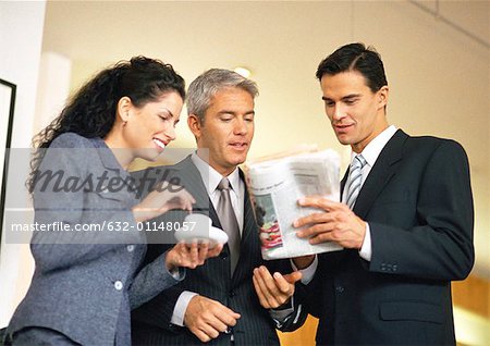 Group of business people looking at newspaper together, waist up, low angle view