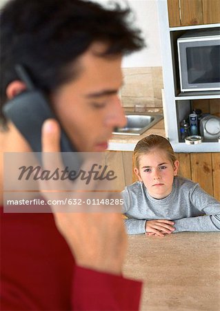 Child looking at father on the phone in kitchen, blurred.