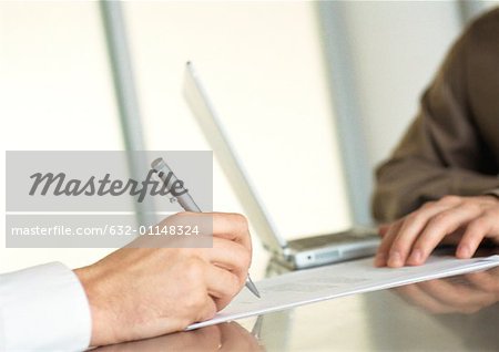Businessman writing and second business man sitting with laptop, close up of hands