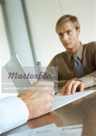 Businessman sitting across from second businessman, close-up of hand writing