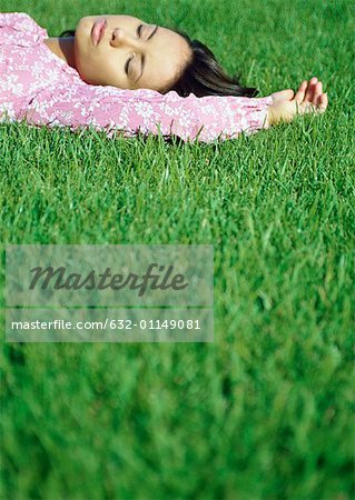 Woman lying on grass with eyes closed, surface level view