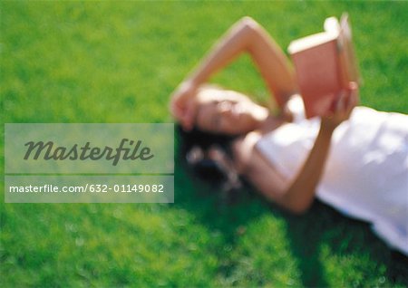 Woman lying on grass, reading, defocused