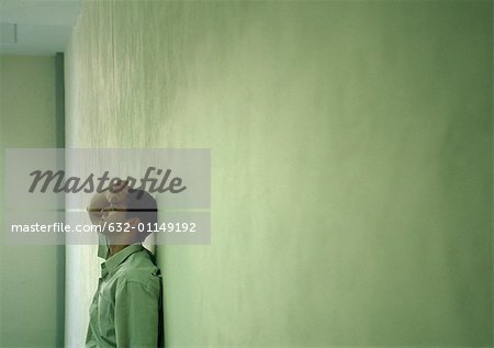 Man leaning against wall, holding head, long shot