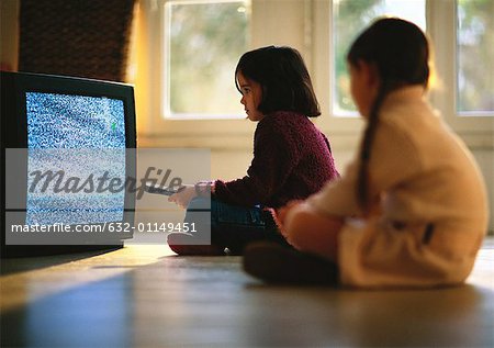 Young girls sitting on wood floor watching TV, girl in foreground blurred