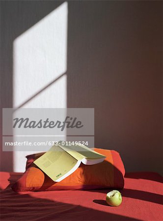 Open book on pillow next to apple