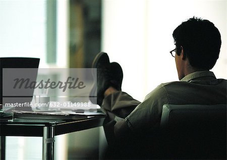 https://image1.masterfile.com/getImage/632-01149988em-man-sitting-in-chair-with-feet-on-table-rear-view-stock-photo.jpg