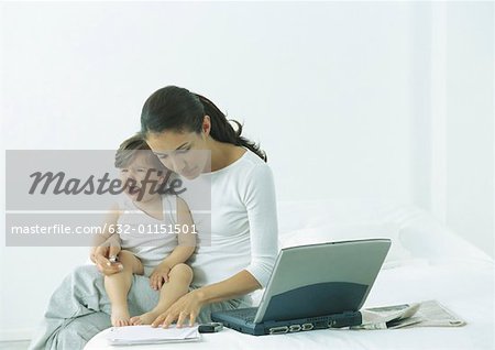 Woman sitting on bed with little girl on lap crying, looking down at paper