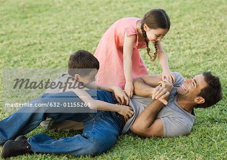 Boy and girl tickling father on grass