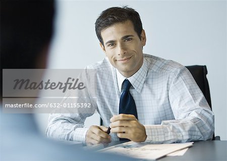 Businessman sitting at desk across from second man, looking at camera