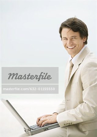 Businessman using laptop, smiling at camera