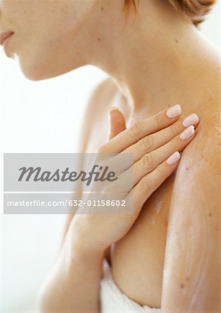 Young woman applying moisturizer to shoulder