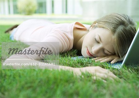 Teen girl sleeping with head on laptop, lying in grass