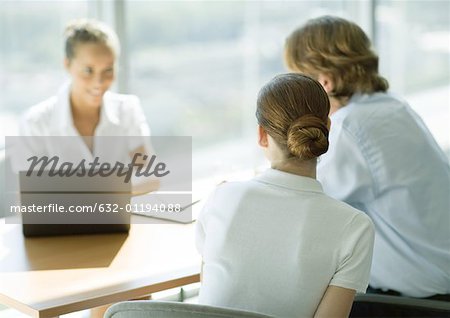 Man and woman sitting across table from smiling businesswoman, rear view