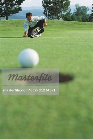 Golf ball at edge of hole, golfer in background squatting down, watching ball