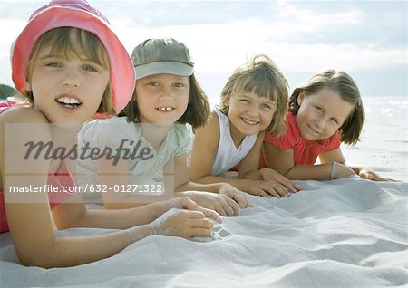 Four girls lying on beach, smiling at camera, close-up