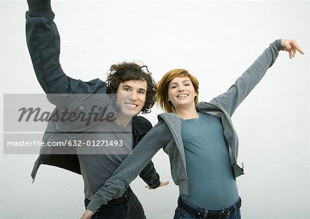 Young man and young woman dancing with arms out, smiling at camera