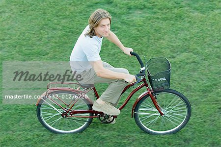 Young man riding bicycle on grass, high angle view