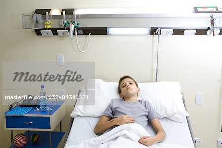Boy lying in hospital bed, holding stomach
