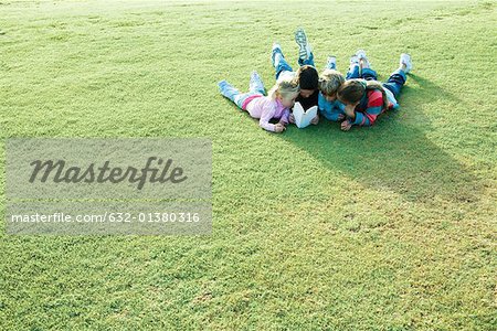 Children lying on grass, reading book together