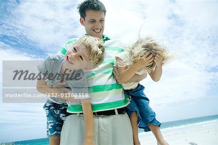 Man carrying son and daughter on beach